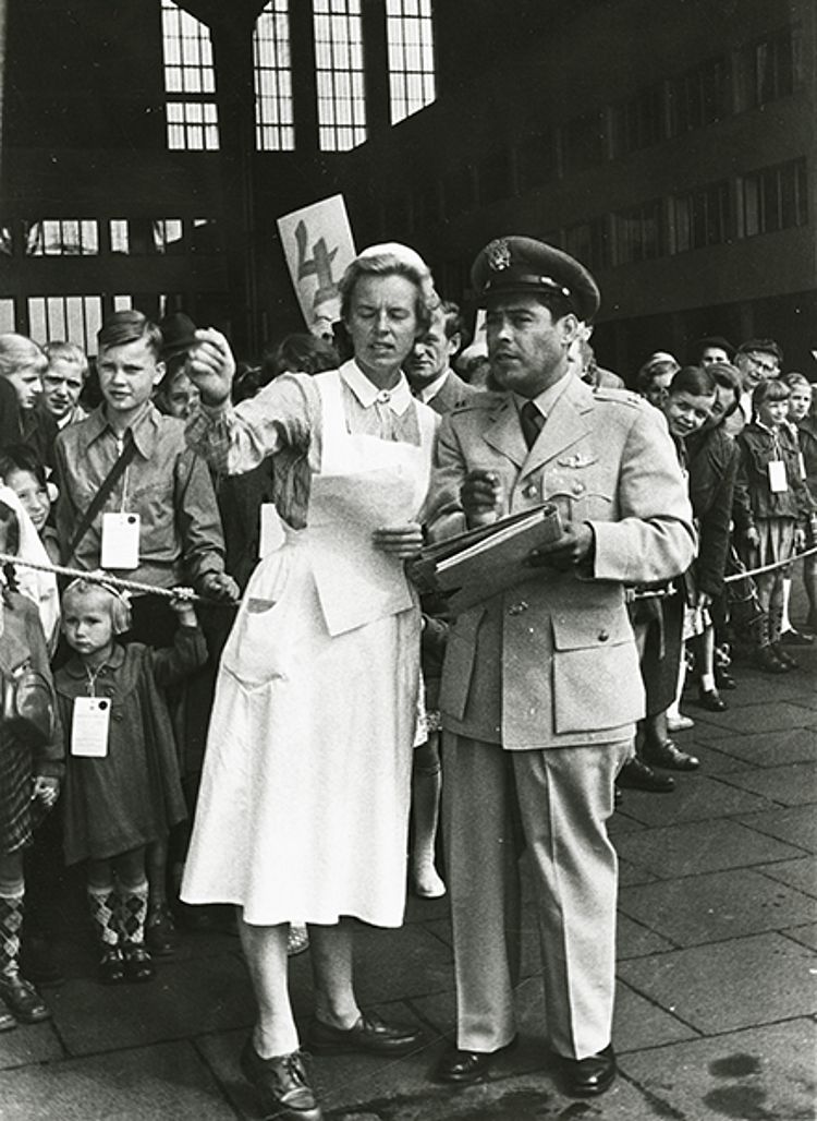 Eine Gruppe Kinder mit einer Betreuerin vom DRK und einem Offizier der US-Luftwaffe auf dem Flughafen Berlin-Tempelhof vor dem Abflug